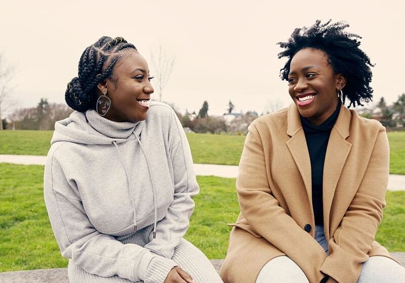 Two women sitting on a bench smiling at each other.